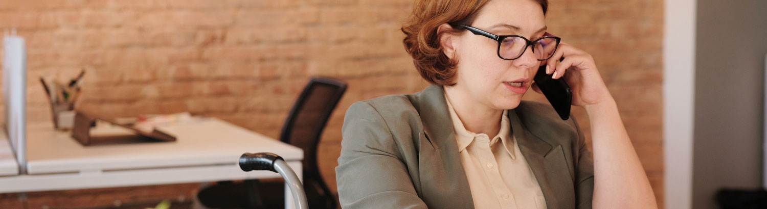 Women using a wheelchair sitting at a desk using a laptop and talking on her smartphone